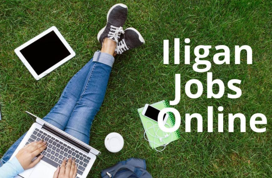 Taong nasa damo gamit ang laptop, may tablet, telepono, at notebook sa malapit. Teksto: Mga Trabaho sa Lungsod ng Iligan Online.