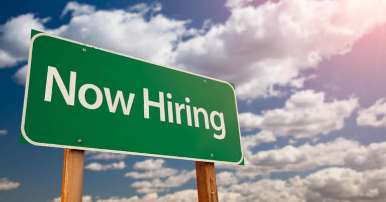 Green Now Hiring sign under Iligan Citys partly cloudy sky with sunlight streaming in from the top right corner.