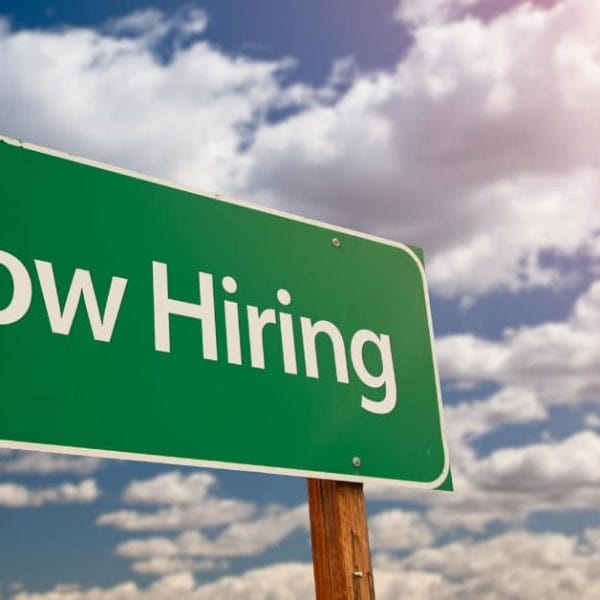 Green Now Hiring sign under Iligan Citys partly cloudy sky with sunlight streaming in from the top right corner.