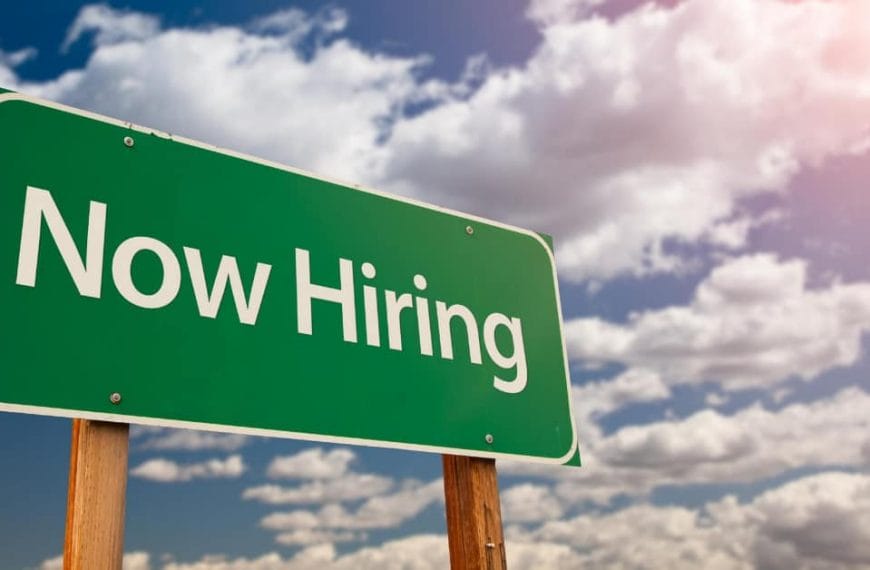 Green Now Hiring sign under Iligan Citys partly cloudy sky with sunlight streaming in from the top right corner.