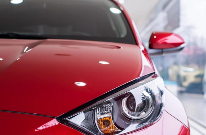 Close-up of a shiny red cars front corner, spotlighting its headlight and side mirror in an Iligan car showroom.