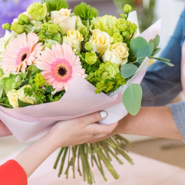 Hands exchange a bouquet of pink gerberas and yellow roses, wrapped in pink paper, crafted by an Iligan flower shop.
