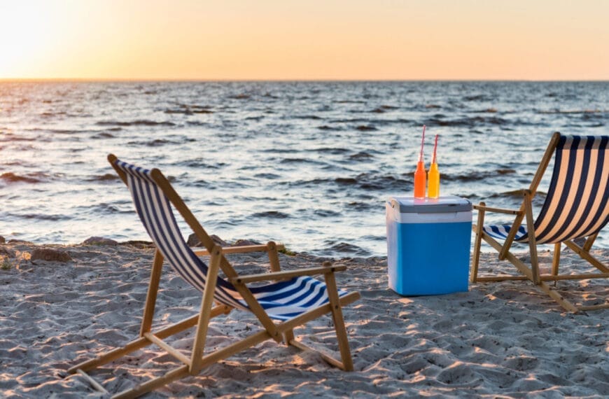 Two striped beach chairs on Iligans sandy shore, a cooler with orange drinks, ocean waves, and sunset sky.