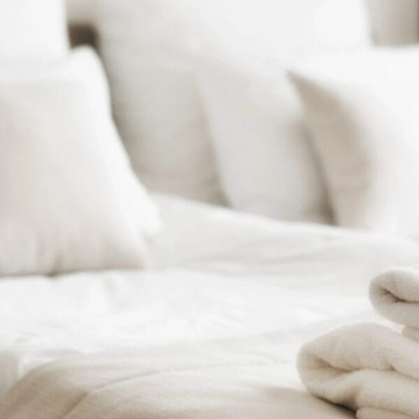 Soft focus of a neatly made bed with white pillows in a bright Iligan hotels room, folded towels included.