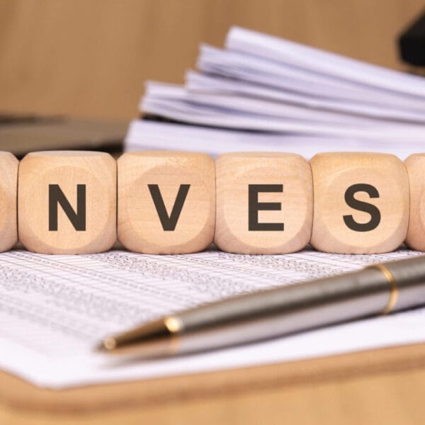 Wooden blocks spelling INVEST ILIGAN on papers with a pen and stacked files in the background.