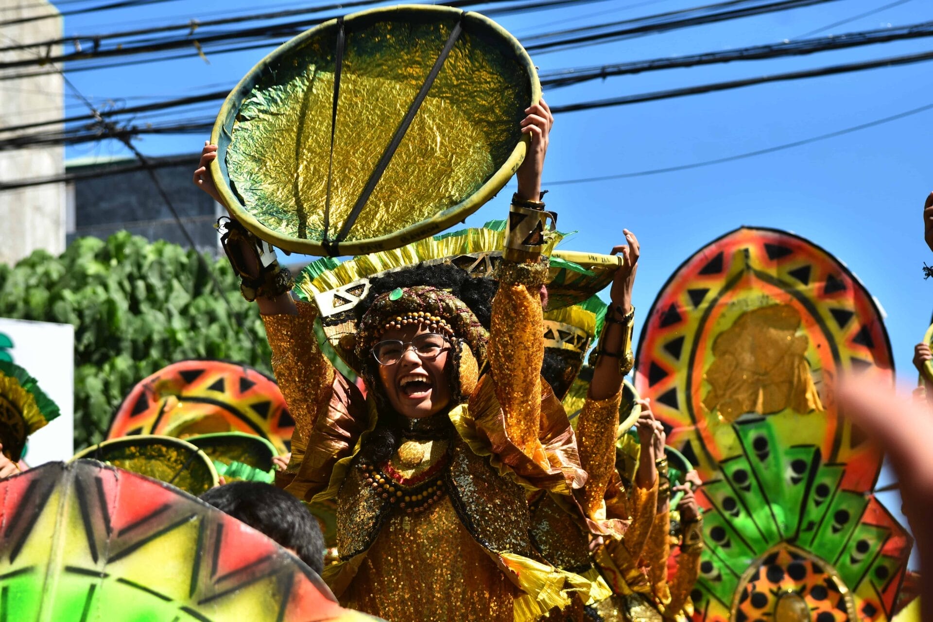 a person in a vibrant costume joyfully holds a large gold prop at the front page template parade