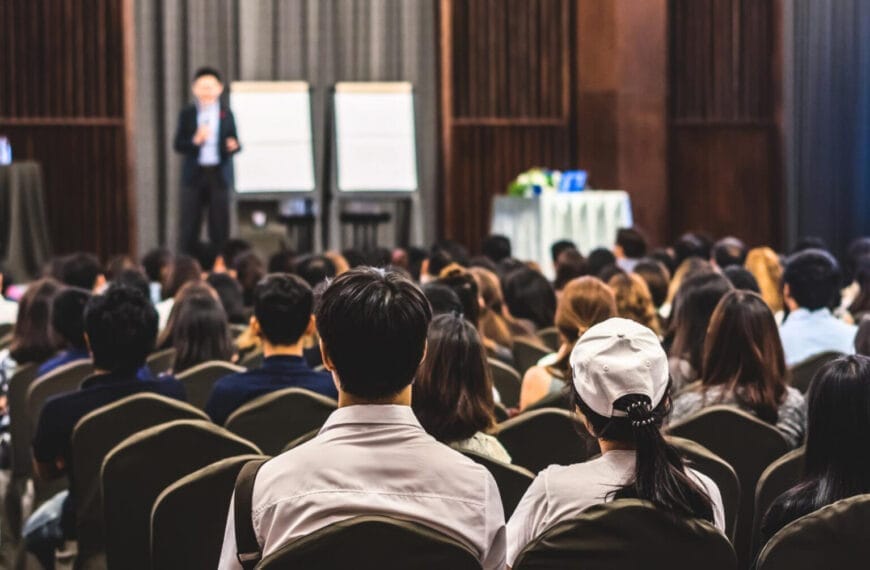 audience seated in rows listens to two speakers at an iligan mice establishment with flip charts.