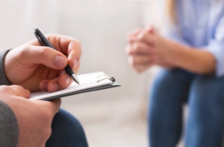 close up of a northern mindanao psychiatrist writing on a clipboard while a person sits across, hands clasped.