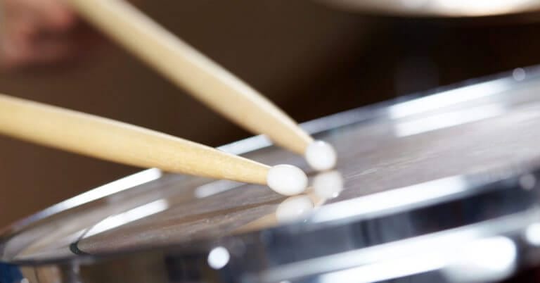 two wooden drumsticks striking a shiny snare drum at the diyandi festival drum and lyre competition.