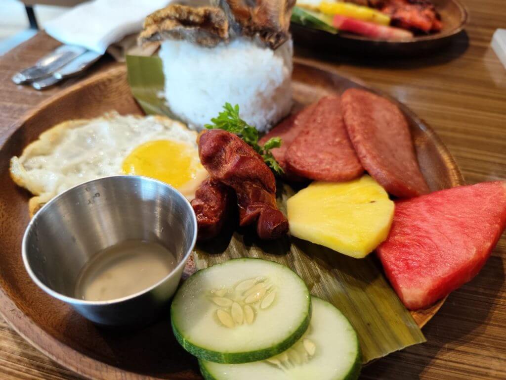 a wooden plate with rice, fried egg, sausage, and more&mdash;perfect for any meal at urban coffee studio open 24/7.