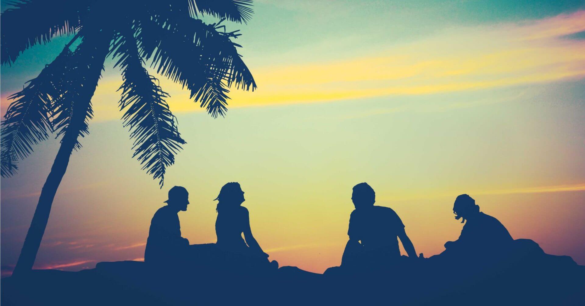 four people sit under a palm tree at sunset, dreaming of their next iligan city travel adventure.
