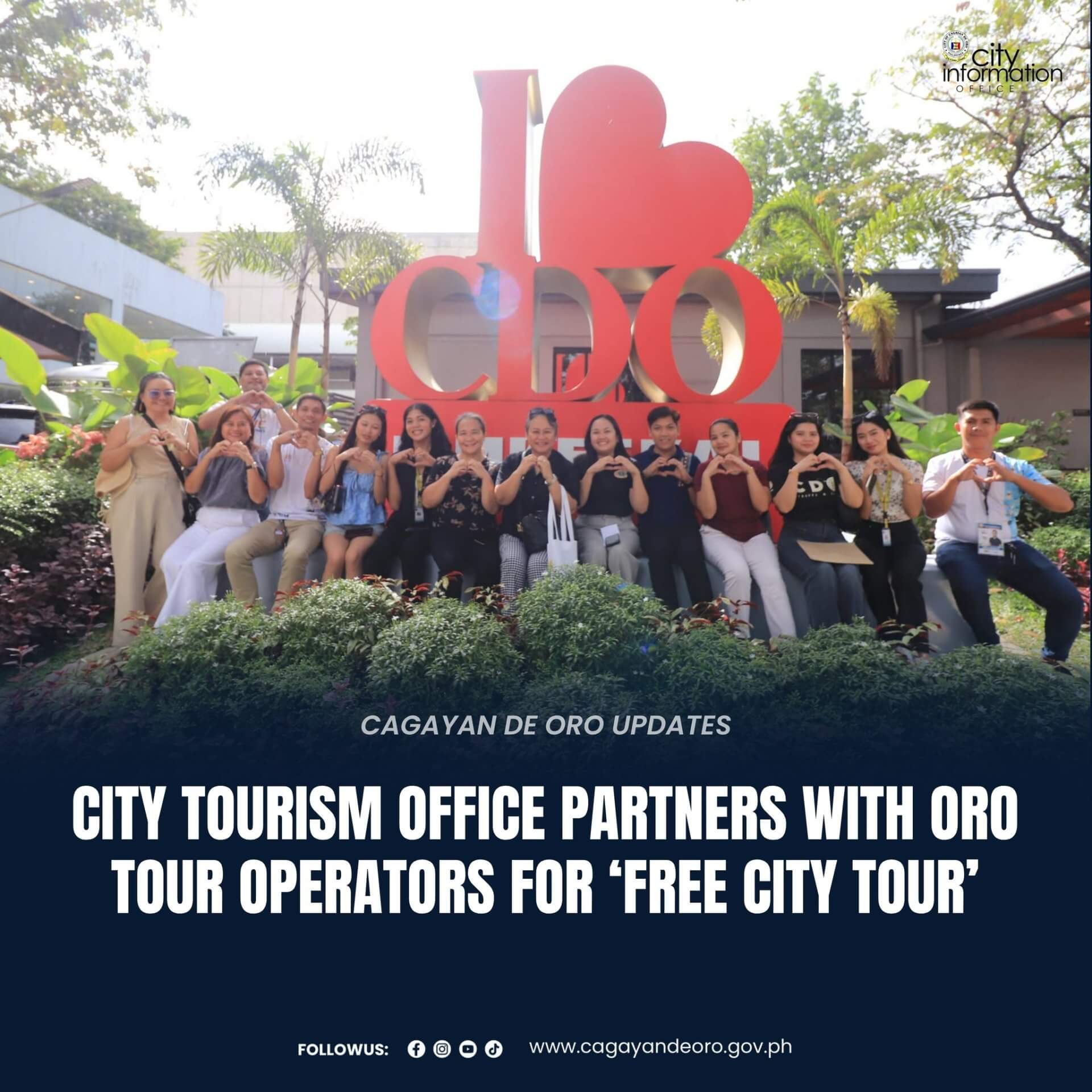 sixteen people sit by a large i love cdo sign, enjoying an outdoor city tour with lush green plants.