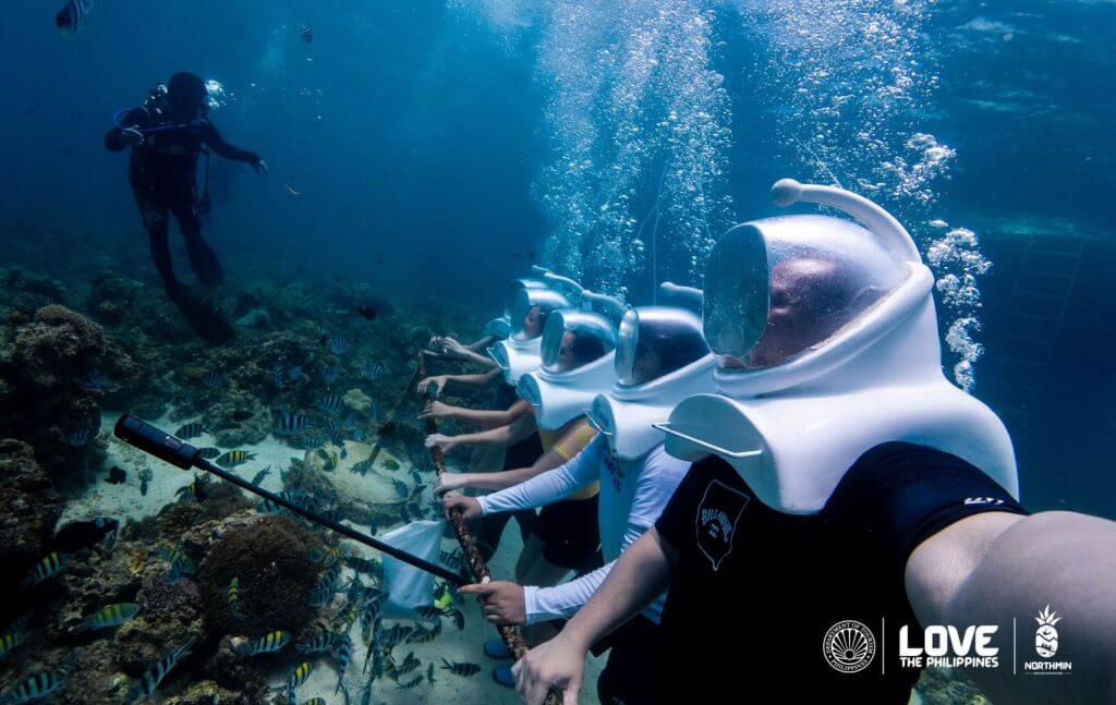 helmet divers explore camiguin's underwater heritage among fish and corals; a diver supervises. love the philippines.