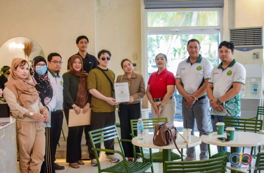 Halal Certified - meku coffee, some smiling with documents; tables and chairs are in front of them.