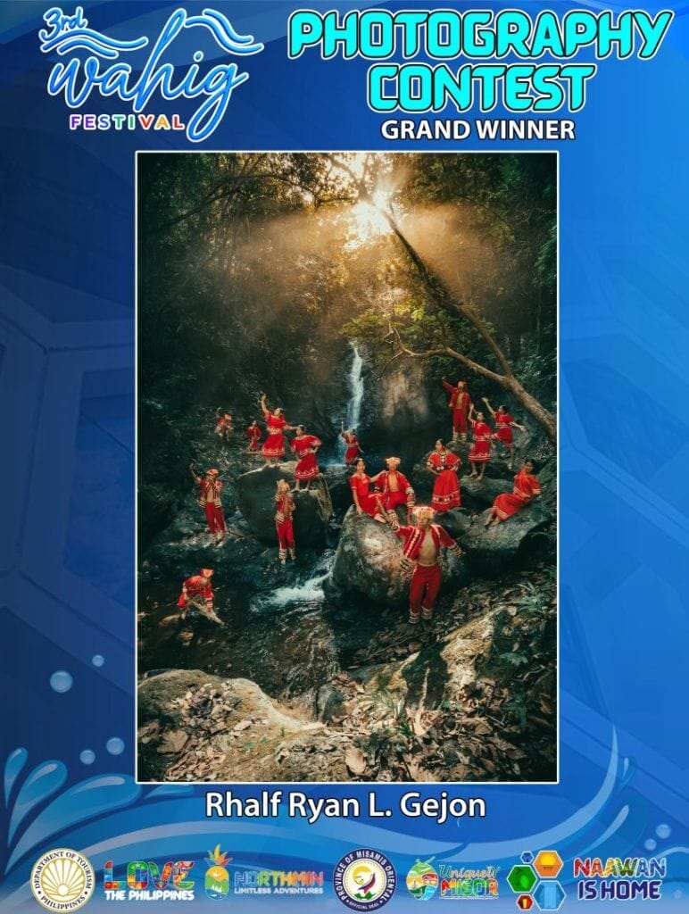 a group in red outfits poses on rocks by a forest waterfall, sunlight streaming through the trees.